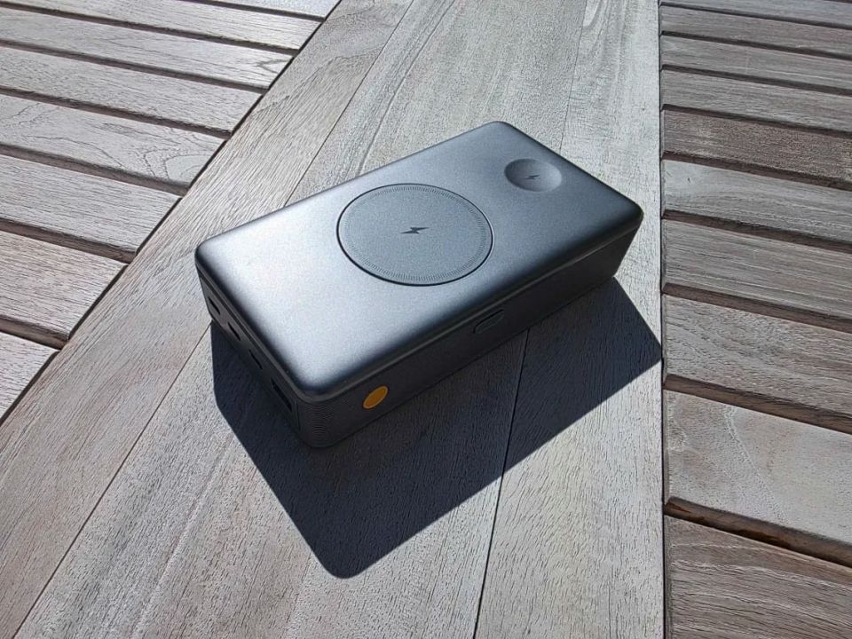 Close up photo of a gray plastic battery brick with USB ports and buttons visible resting on a wooden table.
