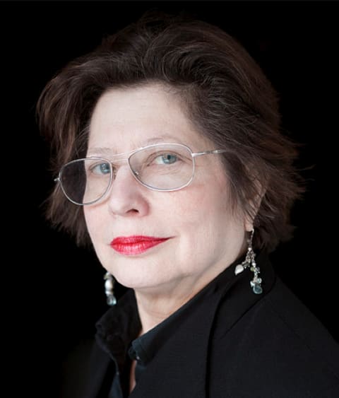 A portrait of a woman standing in front of a black background with dark hair and blue eyes.