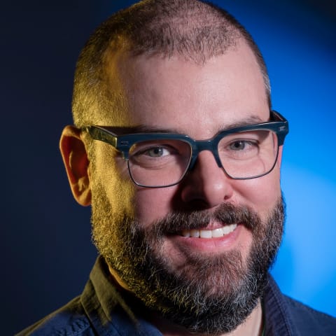 Portrait of Nathan Fox against a bright blue background, lit from one side by a yellow light