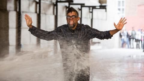 A man with glasses getting sprayed with water.