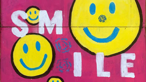 Mural with word "Smile" written vertically five times, partially intersected by four smiley faces of differing sizes.