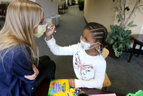 Child painting with markers on a face mask worn by a therapist