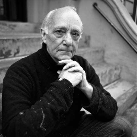 A black-and-white portrait photograph of a man sitting on the steps of a building stoop.