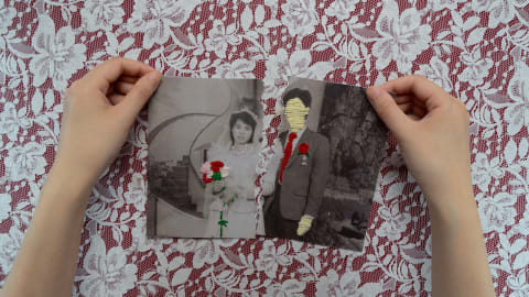 Person holding ripped wedding photograph with the bride in full view and the groom embroidered over with thread