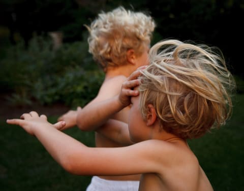 A photograph of two young children running, one with their hand on the other's face.