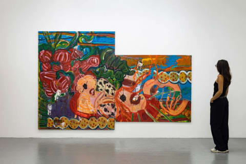 An installation photo of a large, colorful painting hanging on a white wall with a person standing next to the painting, looking at it