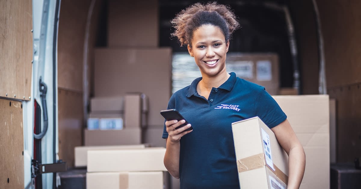 Portrait of a woman holding a package in front of delivery van.