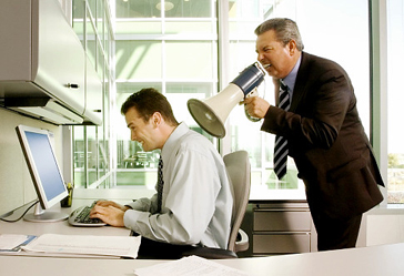 A man shouts into a megaphone just behind a long-suffering developer working at a computer