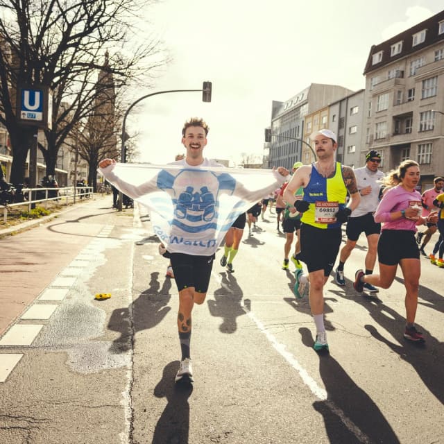 Eine Person vom Sea-Watch Running Team läuft den Berliner Halbmarathon mit Sea-Watch Flagge.