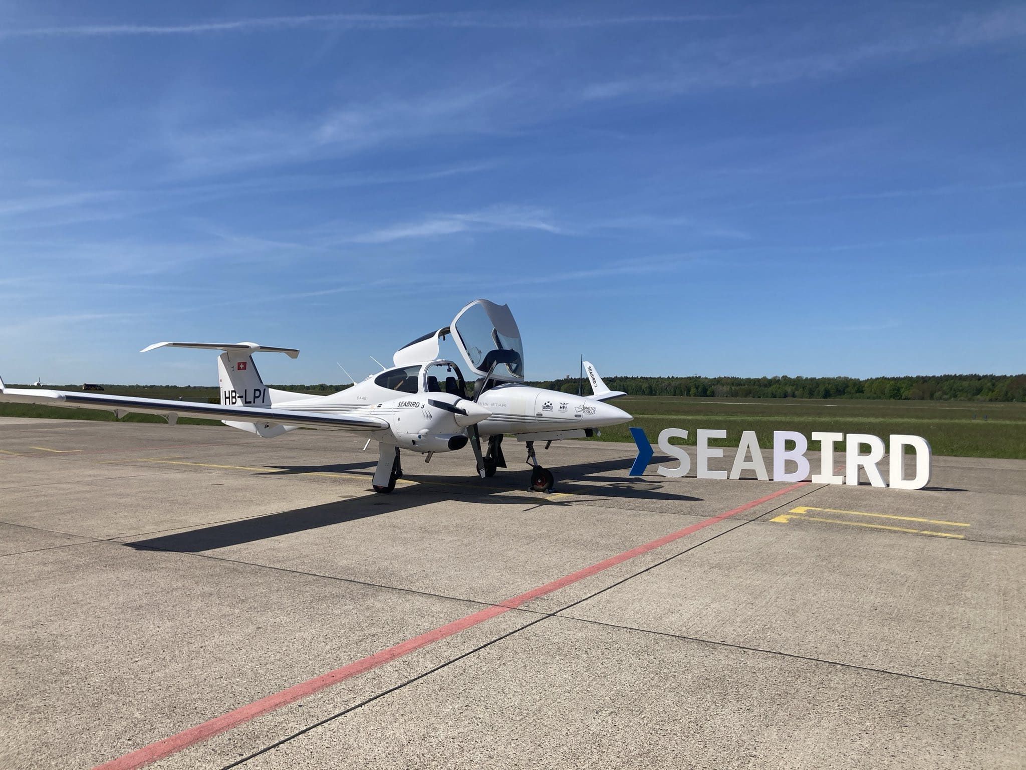 Das Flugzeug "Seabird 3" steht auf dem Flugplatz, daneben ist ein großes „SEABIRD“-Schild zu sehen, während der Himmel klar und sonnig ist.