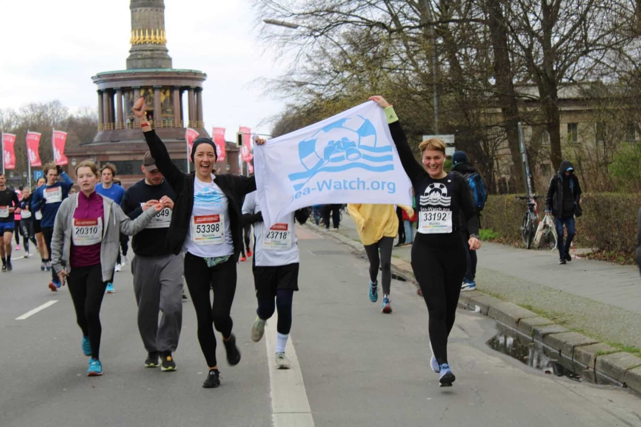 Menschen Laufen den Halbmarathon in Berlin und halten dabei eine Sea-Watch-Fahne in die Luft