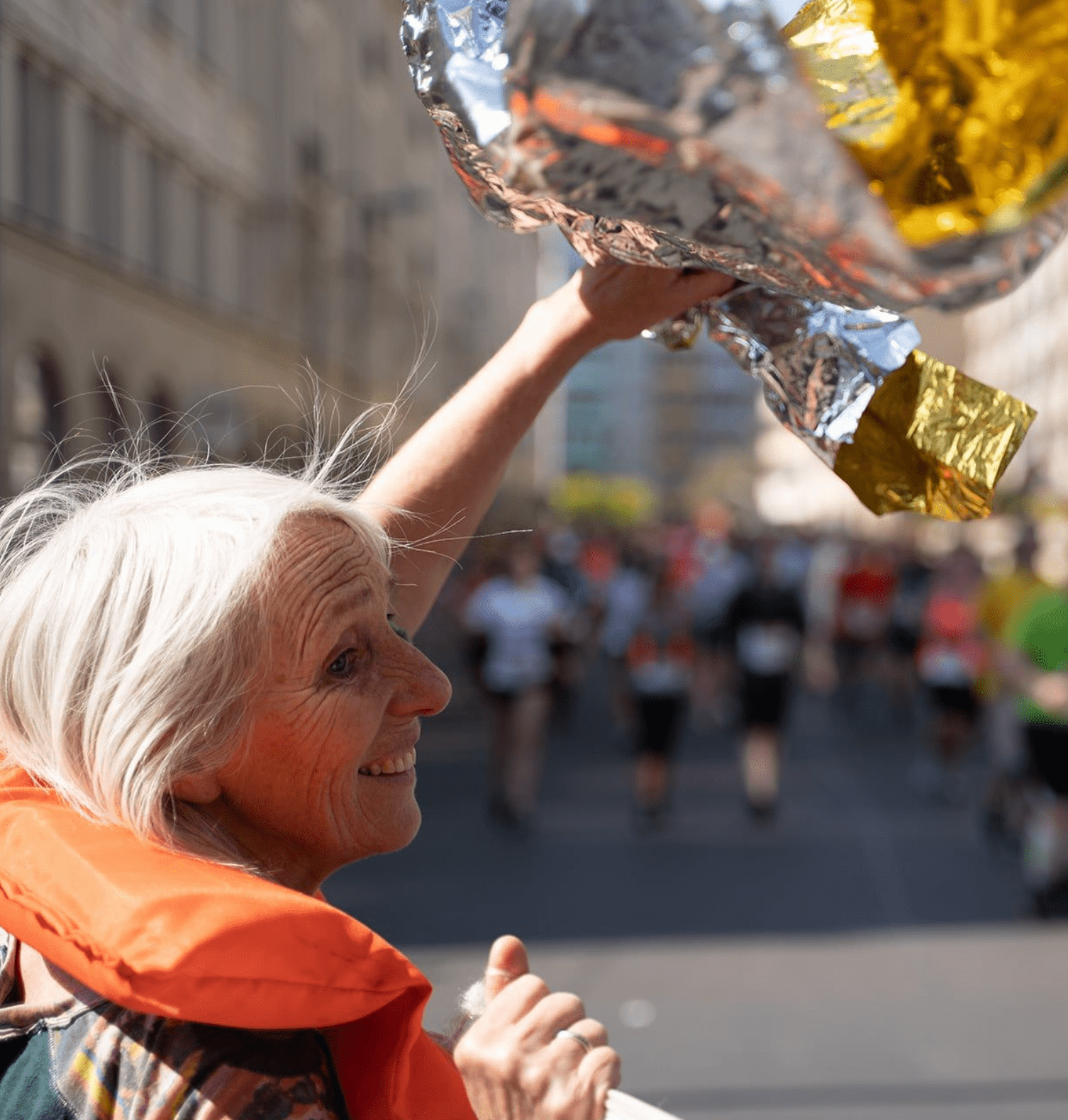 Eine Frau feuert Läufer:innen beim Marathon in Berlin an. Sie trägt eine Rettungsweste und lächelt.