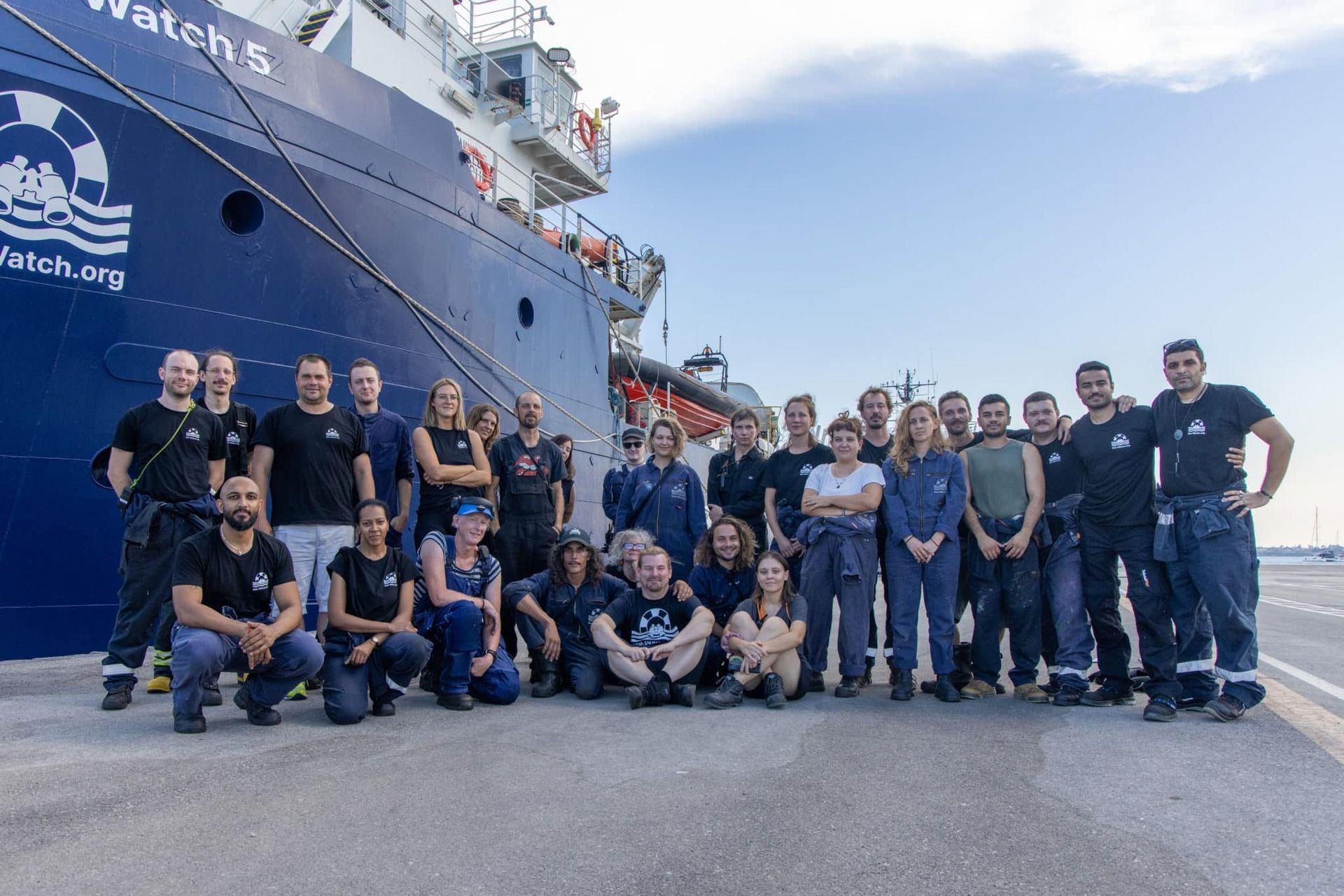 Gruppenfoto der Crew im Hafen, im Hintergrund die Sea-Watch 5