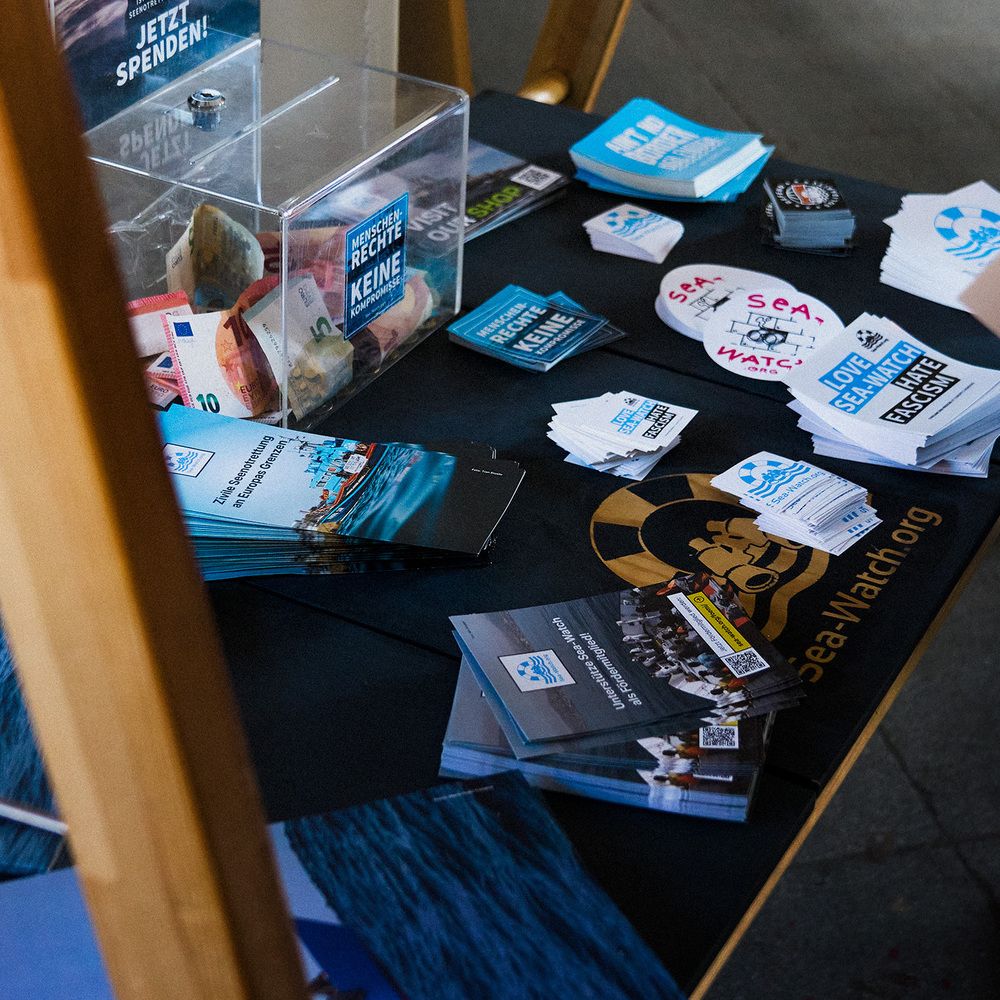 Eine Spendenbox und Sticker von Sea-Watch auf einem Tisch.