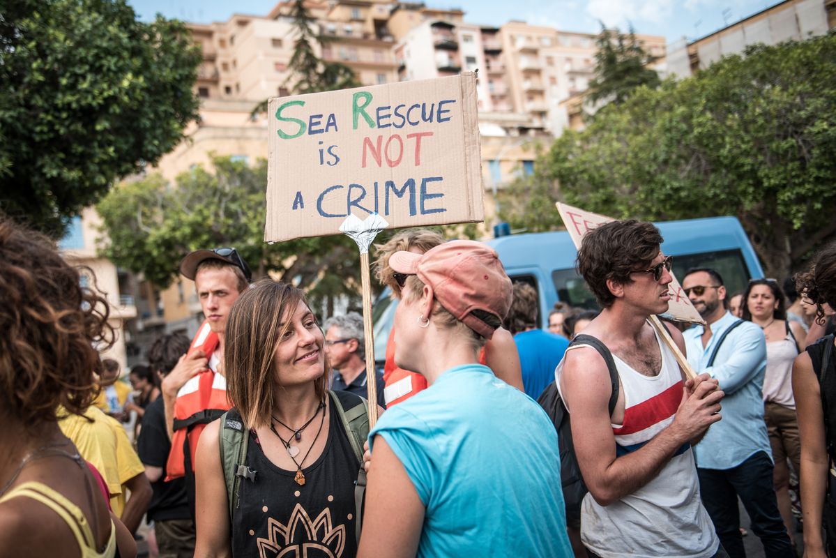 Mehrere Menschen auf einer Demo, im Vordergrund zwei Personen mit einem Schild: "Sea-Rescue is not a crime."