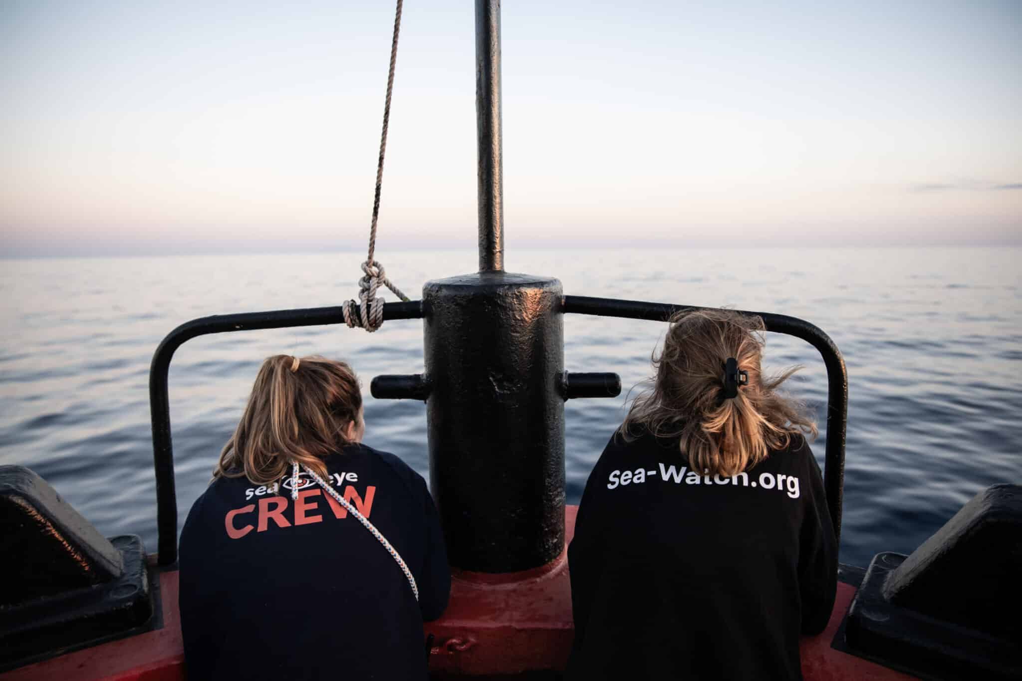 Zwei Crewmitglieder blicken vom Heck eines Schiffes auf das ruhige Meer im Abendlicht.