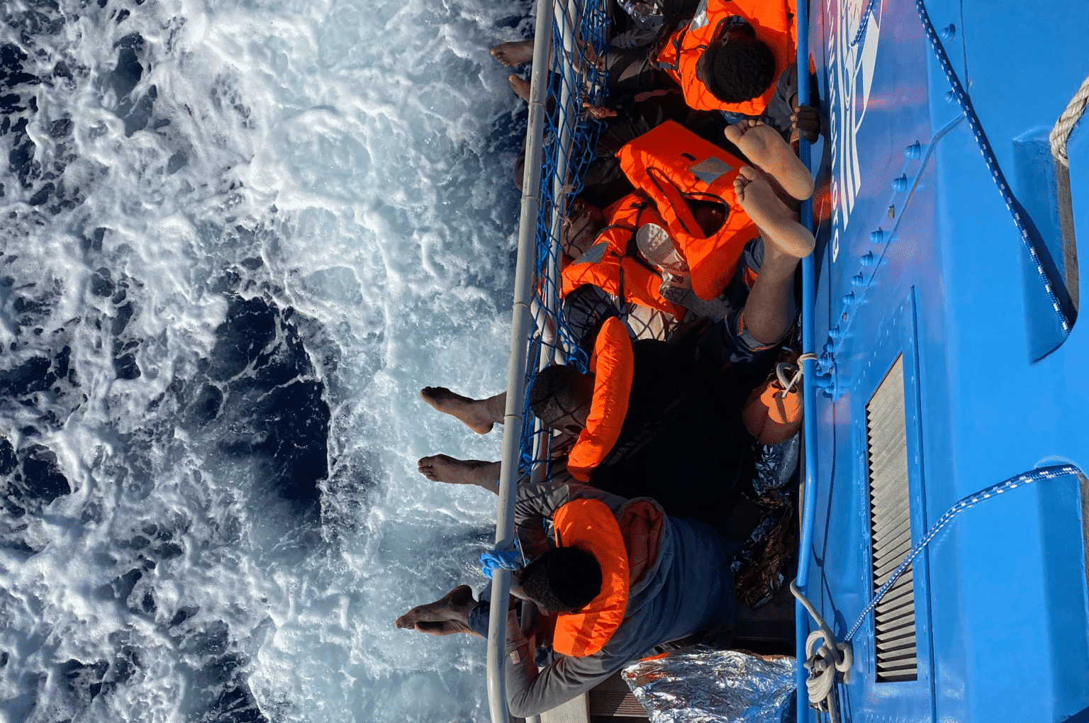 Gerettete in Rettungswesten sitzen an Bord der Aurora 1 und blicken auf ein schäumendes Meer unter ihnen.