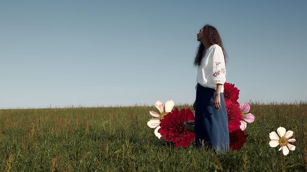 A woman in a sunny field, wearing a Seasalt blouse and trousers.