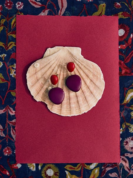 A close up of drop earrings with purple and red beads.