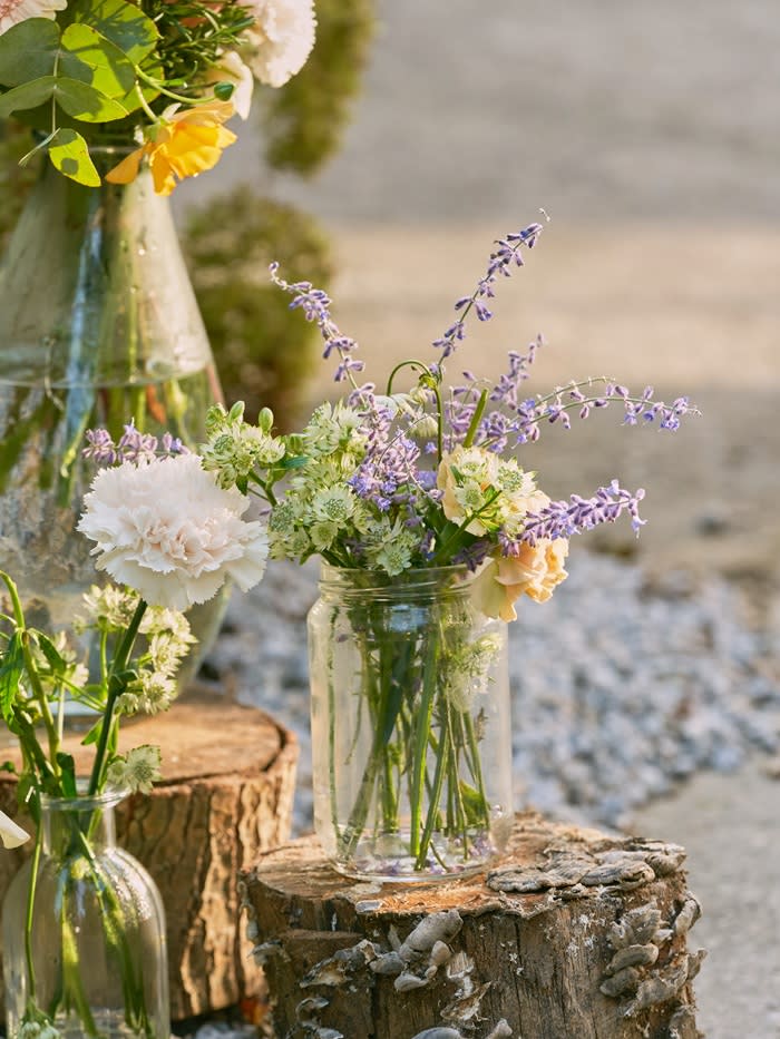 A mason jar of colourful flowers on a log.