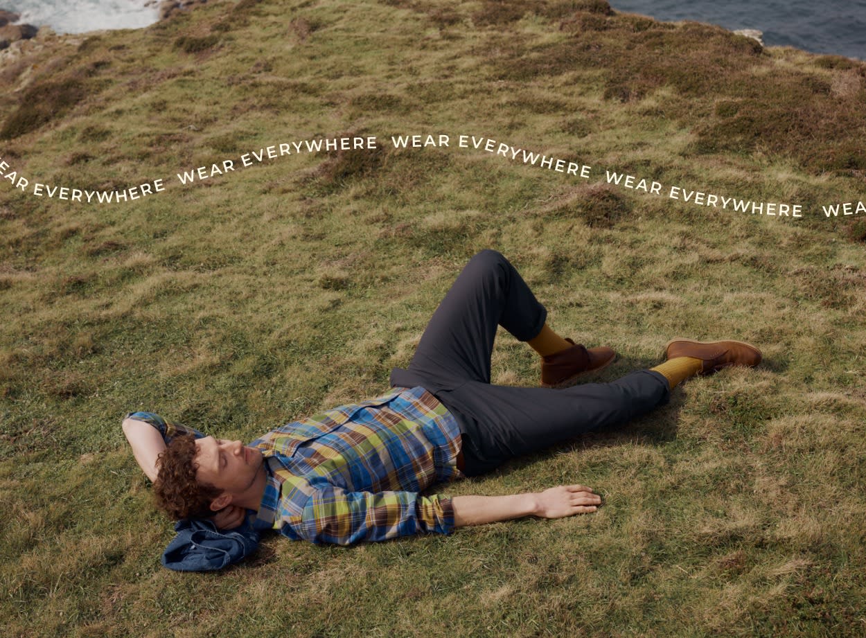 A man reclined on a cliff top wearing a checked Seasalt shirt