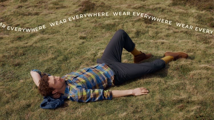 A man reclined on a cliff top wearing a checked Seasalt shirt