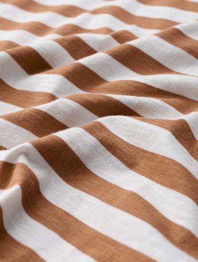 A close up of organic cotton jersey fabric with orange and white stripes