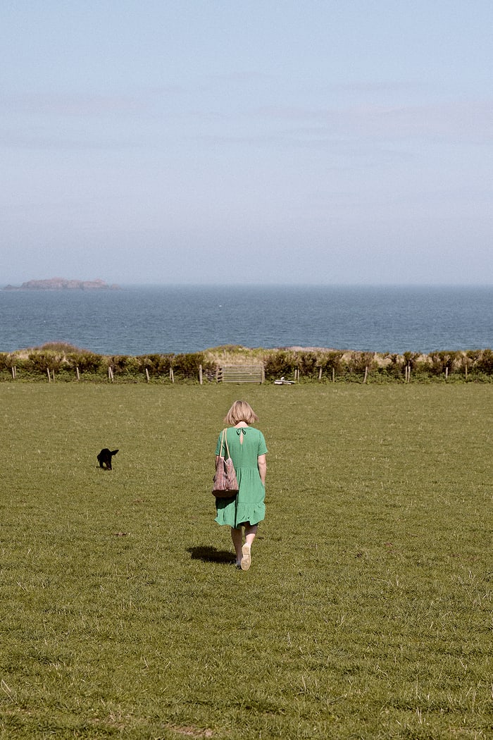 Emily Scott walks across a grassy field to a beach in Cornwall on a sunny day
