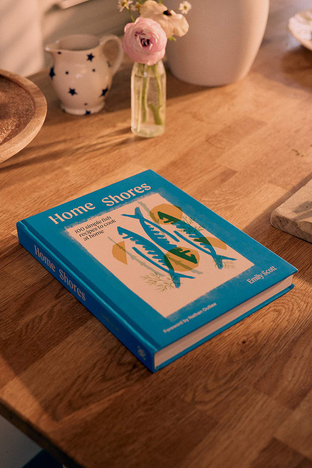 Emily Scott's new cookbook 'Home Shores' on a wooden table with a bunch of flowers