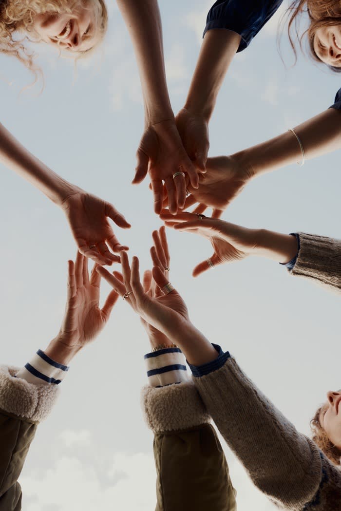 Femmes De La Mer gathered in a group huddle, hands together in the middle