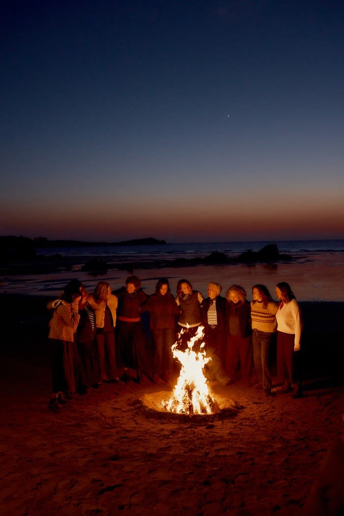 Femmes De La Mer huddled around a glowing bonfire in the dark