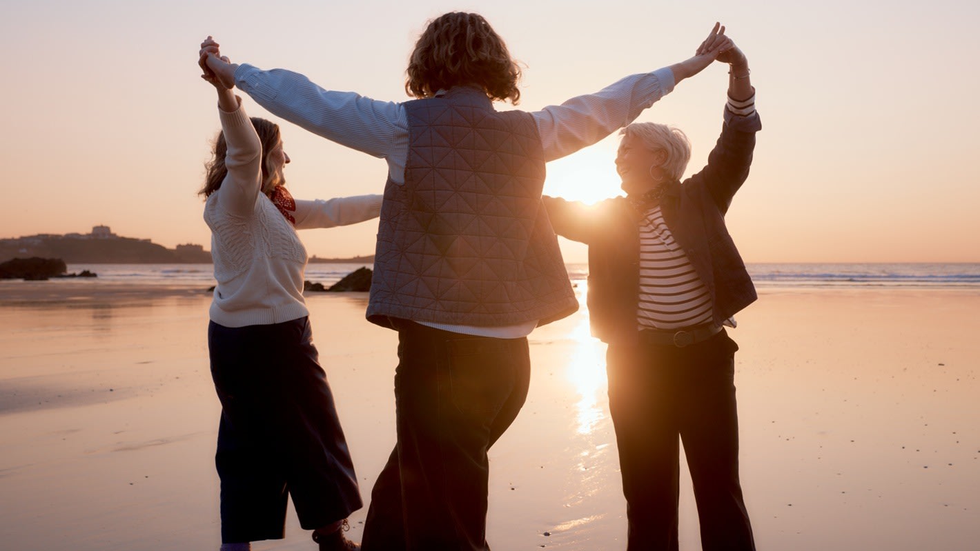 Three members of Femmes De La Mer holding hands, spinning on the beach