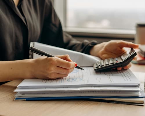 Personne utilisant une calculatrice sur smartphone pour effectuer un calcul financier à côté d’un ordinateur portable sur un bureau