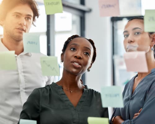 Trois professionnels discutent autour d’un tableau de post-its lors d’une réunion d’équipe, analysant le product market fit de leur projet