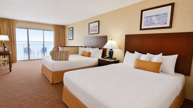 A hotel room with two queen beds, a balcony, and a desk.