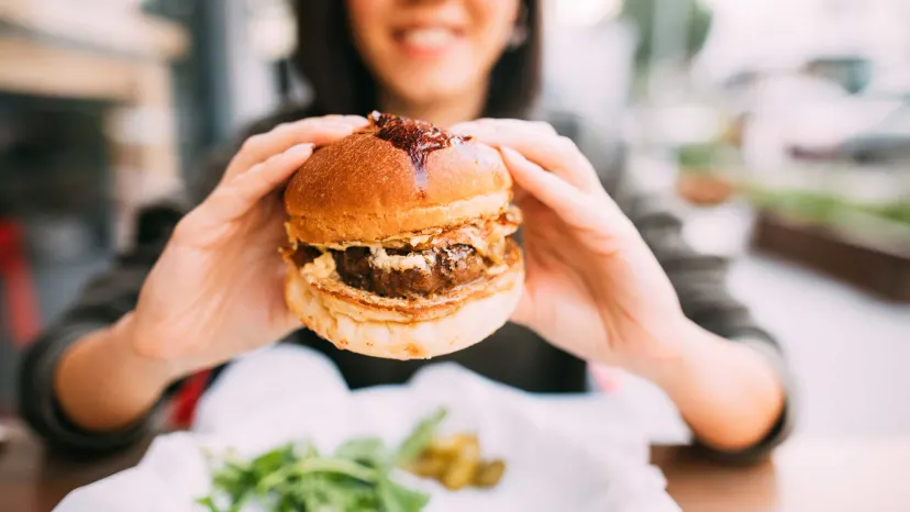 Woman holding a very greasy double cheeseburger.