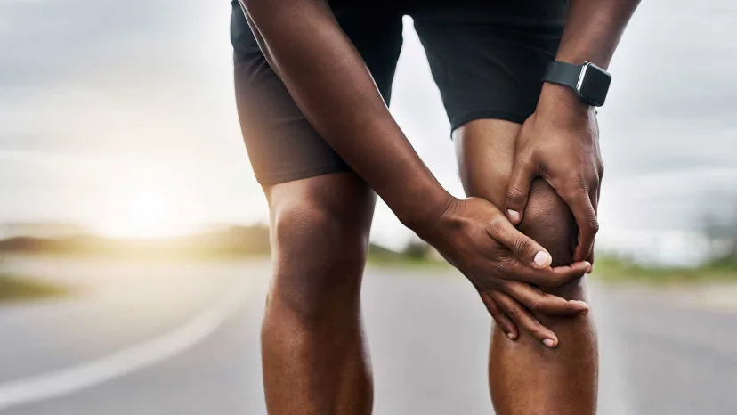 Person holding their knee in pain in the middle of a run.