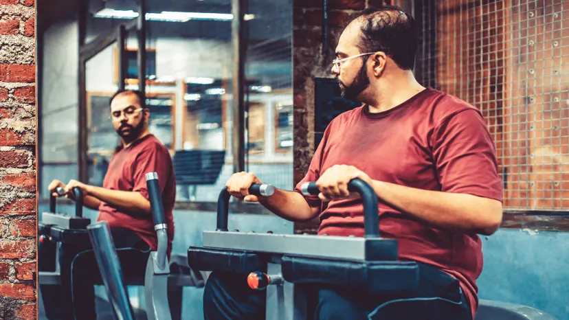 Overweight man working out in a gym and looking in the mirror.
