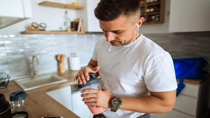 Young athletic man making a smoothing with added supplements.