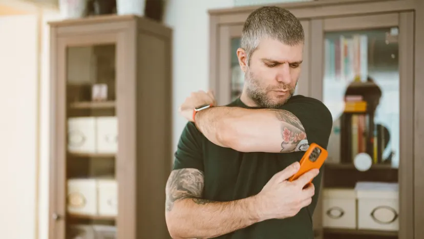man standing at home checking his glucose levels with his arm sensor and smart phone