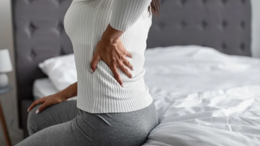 closeup of woman sitting on her bed, holding her back because of Fibromyalgia pain