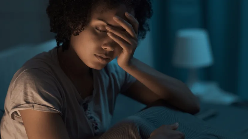Closeup of woman in the darkness of her bedroom, holding her head in her hand because she is experiencing sleep difficulty due to her fibromyalgia