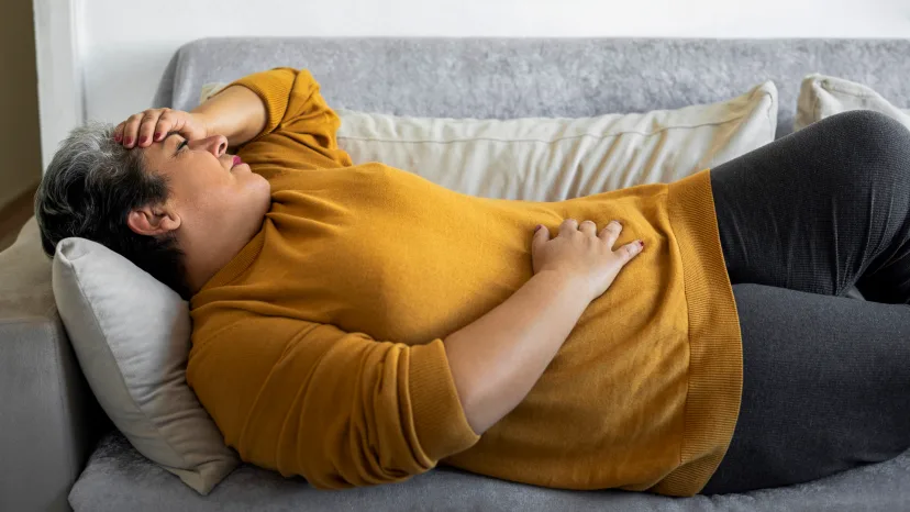 Woman suffering from abdominal pain due to menopause lies back in her couch clutching her stomach.
