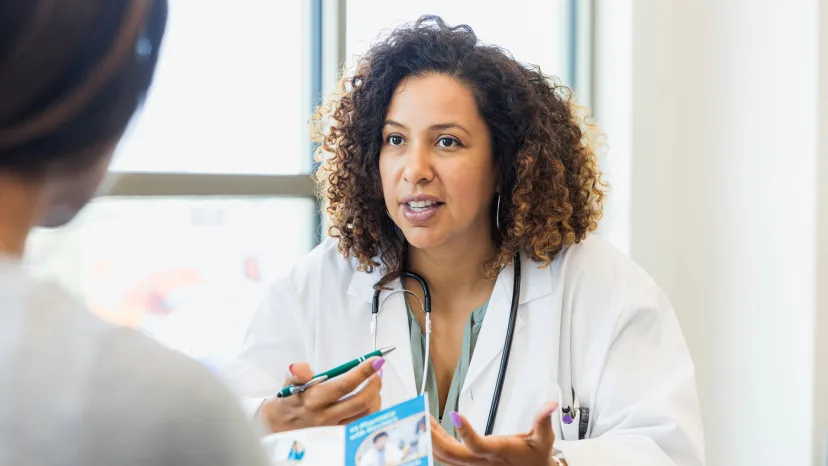 Female doctor in lab coat sits at a desk discussing hepatitis test results with a female patient