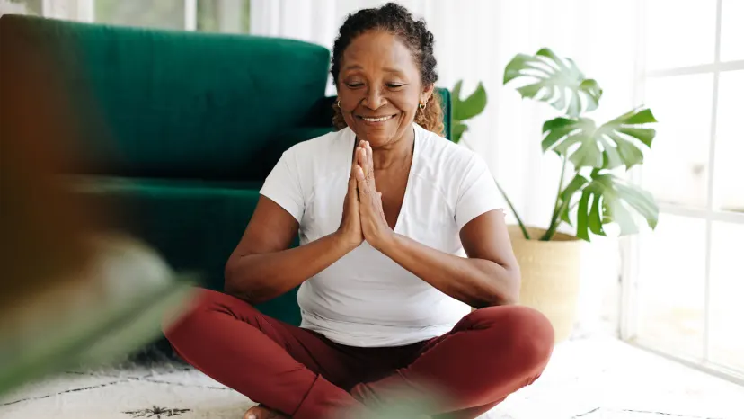 Mature woman with hepatitis sitting cross-legged on a floor holding her hands together with eyes closed practicing yoga