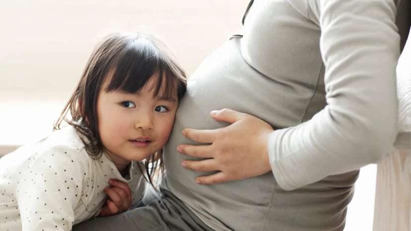 Young girl listening to the belly of her pregnant mother