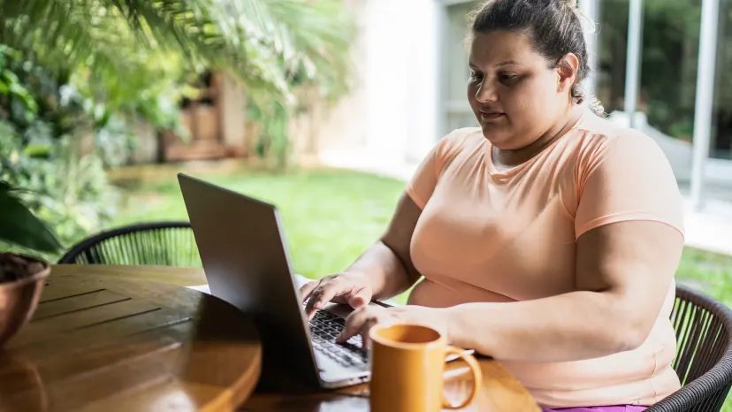 Obese woman typing on a laptop in a backyard garden area