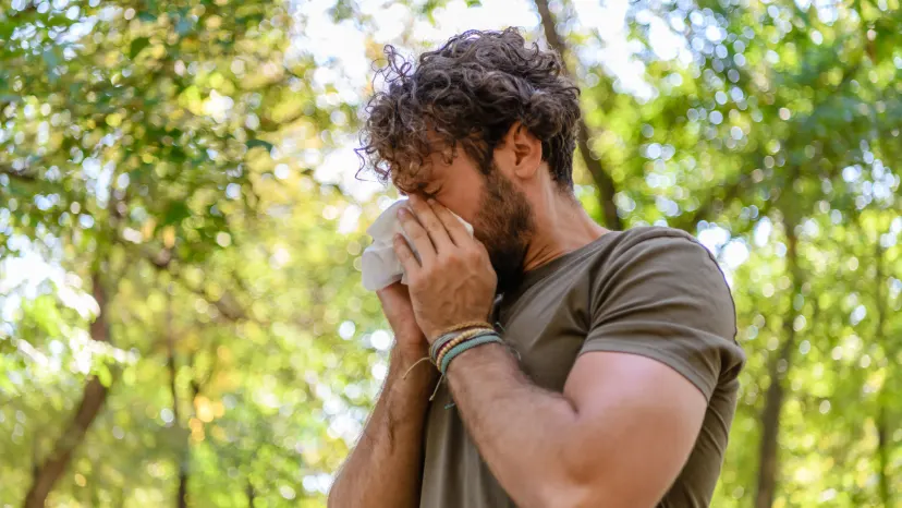 Man suffering from seasonal allergies blowing his nose in a park area