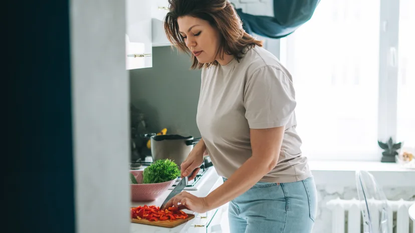 Woman in the kitchen cutting up vegetables for a salad.