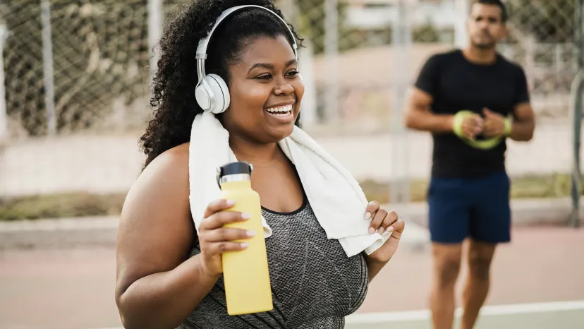 Woman with a water bottle on a basketball court in between workouts.